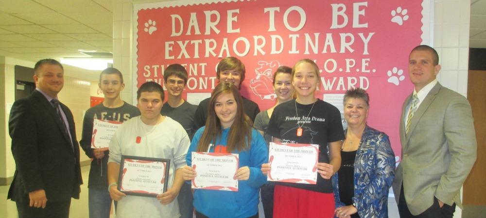 Student of the Month award winners display their certificates in front of the “Dare to be Extraordinary” board.