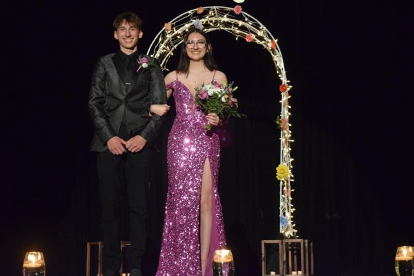 In lights: Standing in front of the archway, senior Skylar Scobbo and junior Elias Boyd pose for pictures during grand march. The stage was decorated with a lit arch, lanterns hanging from the ceiling and floating candles lining the stage.