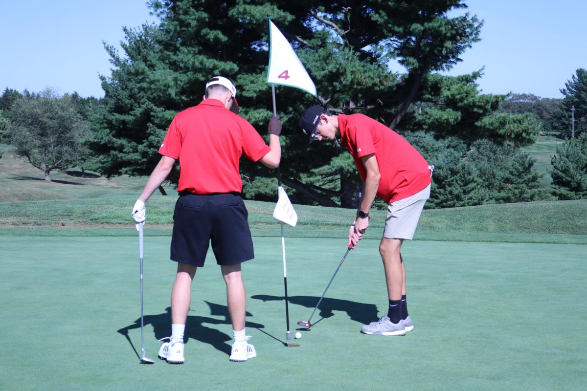 Tee-mates: Preparing to sink the ball, Nicholas Metzger (10) holds the flag as Bryson Deal (11) putts his golf ball on Sept. 3. Players traveled with one team mate and two opposing players throughout the course.
