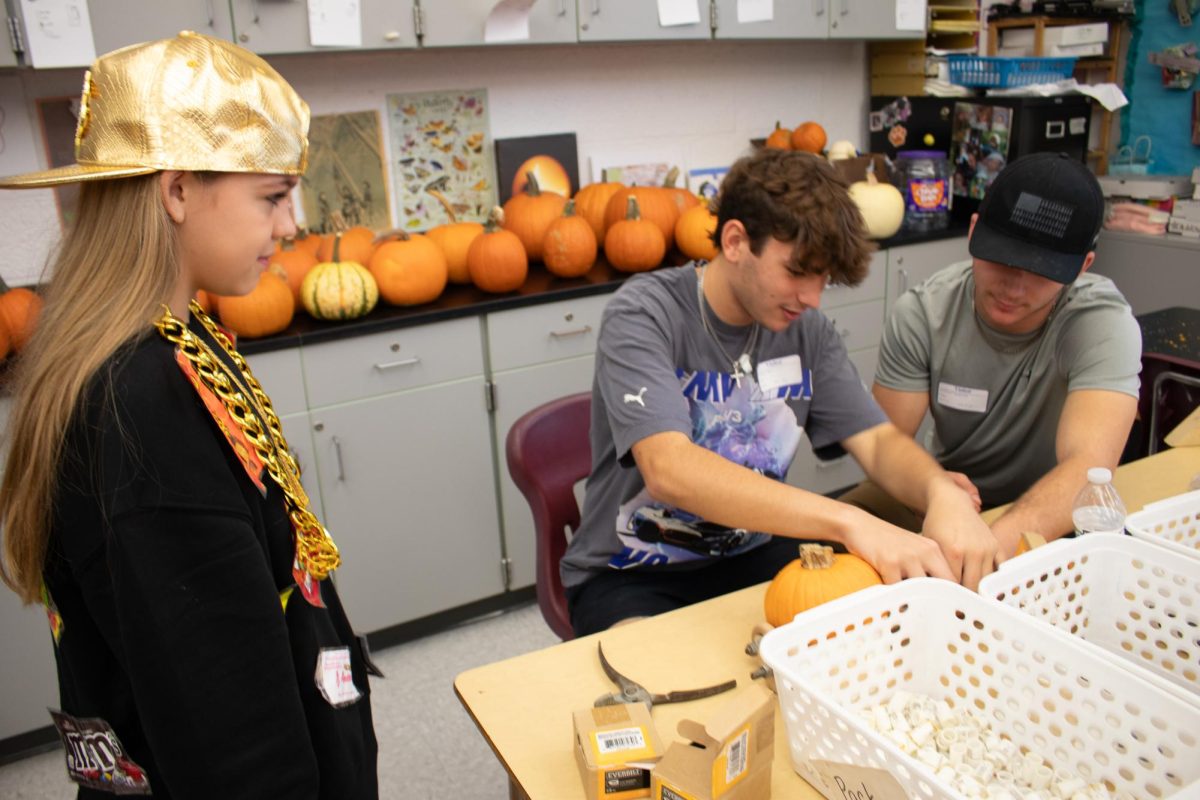 Chop shop: Carving pumpkins, Thomas Ward (12) and Garrett Drutarosky (11) fit axles into the derby cars. Physics Club students prepared all of the drilling and cutting to ensure Fall Fest was as safe as possible for the younger students.