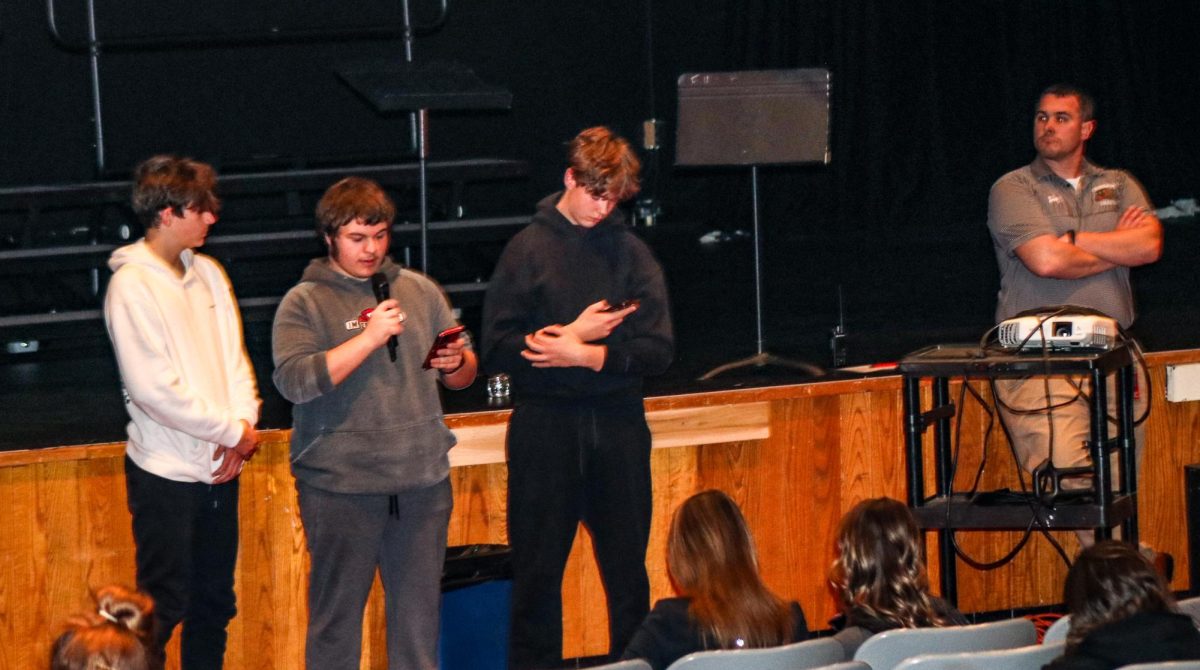 A new world: Reading from his phone, Leo Kaleugher (11) presents his part on the behalf of Physics Club during the club fair. This year’s annual club fair took place on Nov. 25 in the auditorium.