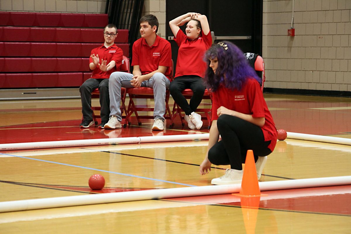 Kneeling down, Hailey Stinar (12) rolls the bocce ball down the court as her teammates watch. During bocce games, all members of the team keep watchful eyes on their peers’ turns to help support and strategize their next moves.